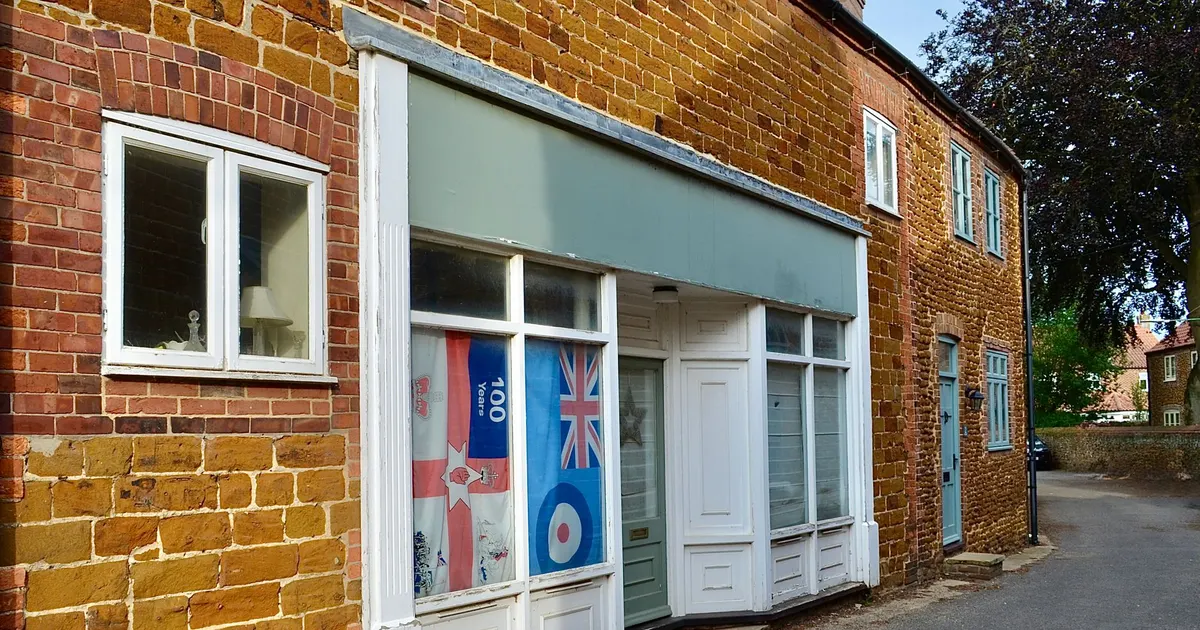 Devanture de commerce de village avec un bandeau d'enseigne vide et une vitrine affichée